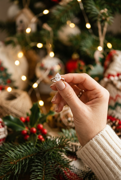 Elegant water drop zircon ring held in a woman's hand against a festive bokeh background of pine and fairy lights
